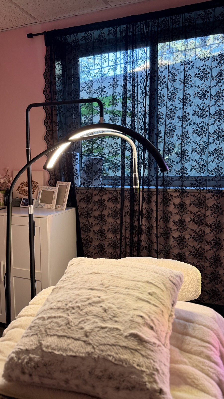 A lash bed with a soft white blanket by the window, lit by a ring light